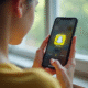 Jeune adulte tenant un smartphone avec Snapchat ouvert affichant un cœur jaune